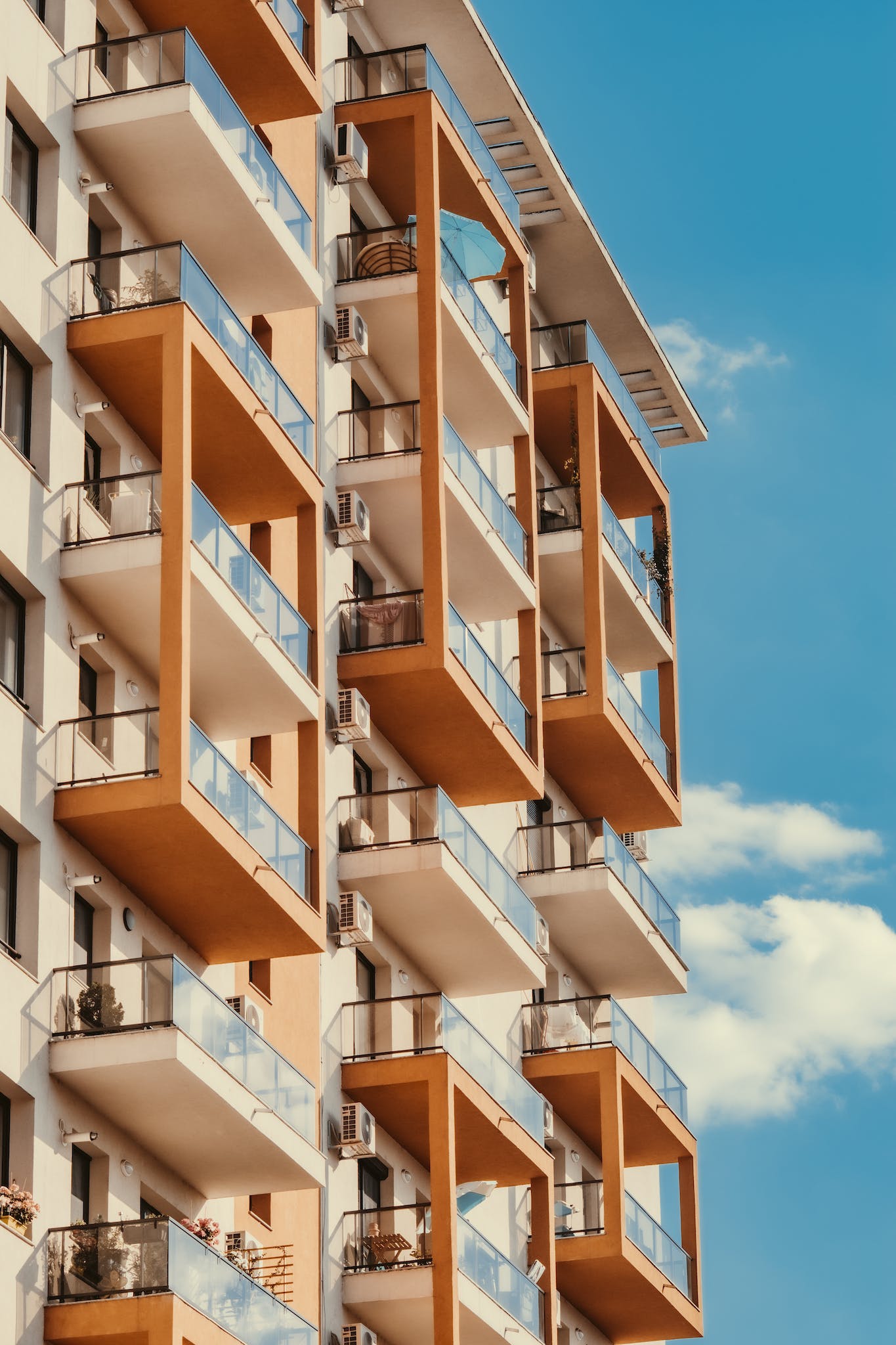 Low angle facade of modern brown and white condominium building with glass balconies against cloudless blue sky